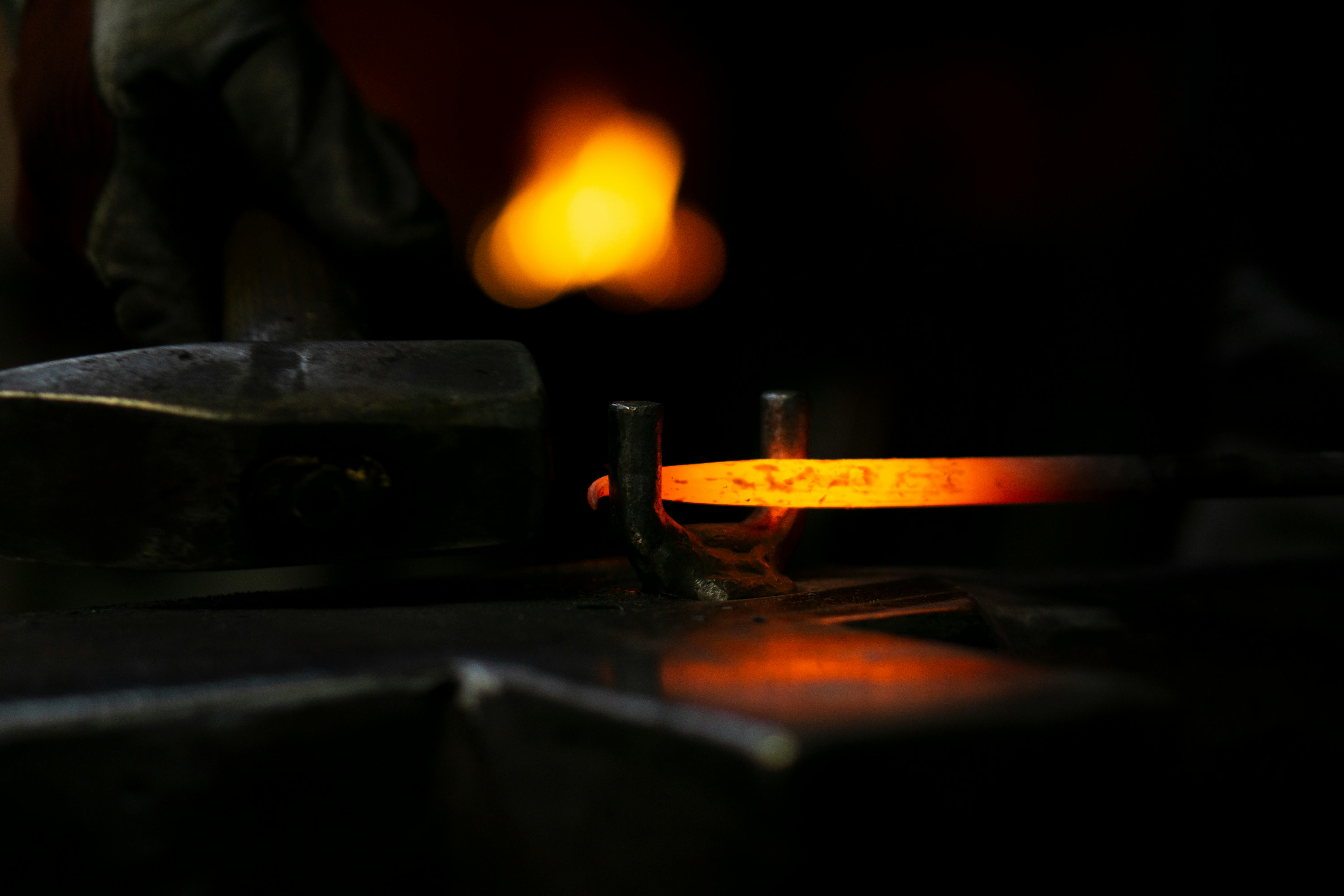 Blacksmith hammering glowing hot iron on the anvil at the forge